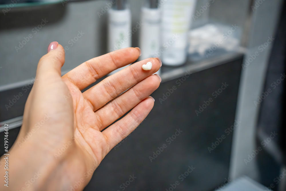 Female hand with cream in the form of a heart on a bath background. Dermatology