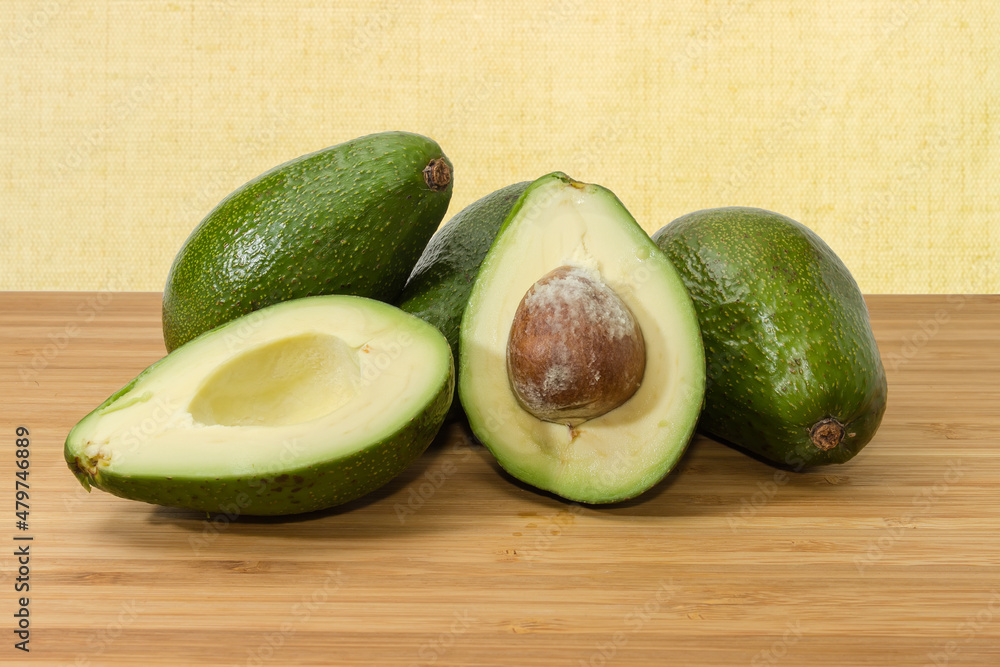 Whole and halved green avocado fruits on a wooden surface Whole and halved green avocado fruits on a wooden surface