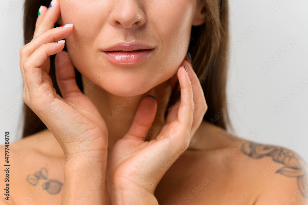 Cropped portrait of lower part of face attractive asian woman with naked tattooed shoulders, is touching face with both hands with colorful manicure. Skincare and bodycare concept