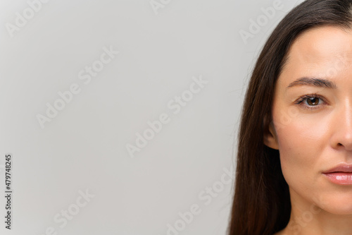 Cropped portrait of attractive asian woman with naked shoulders looking at the camera. Half face of serious beautiful female with smooth face skin and natural make-up, straight healthy hair isolated