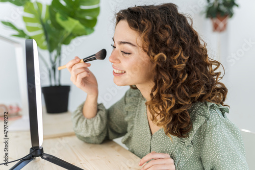 pretty woman with curly hair putting on makeup at home with a brush