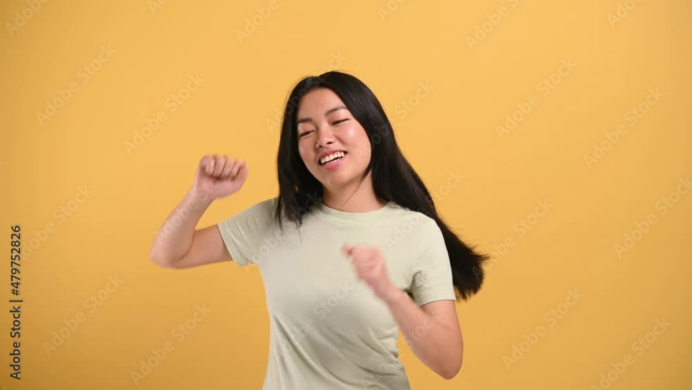 Joy, victory, luck. Cheerful happy chinese brunette girl in casual t-shirt, dancing to favorite music, having fun, rejoice in luck, on isolated orange background Joy, victory, luck. Cheerful happy chinese brunette girl in casual t-shirt, dancing to favorite music, having fun, rejoice in luck, on isolated orange background