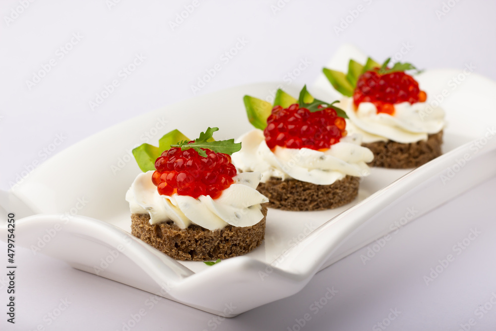 Sophisticated gourmet appetizers featuring rye bread, creamy spread, vibrant red caviar, and crisp avocado slices on a sleek white dish. Sophisticated gourmet appetizers featuring rye bread, creamy spread, vibrant red caviar, and crisp avocado slices on a sleek white dish.