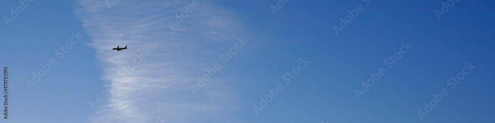 A plane is flying in the distance. Airplane in the air. Blue sky and white clouds. Banner on the theme of passenger transportation or travel A plane is flying in the distance. Airplane in the air. Blue sky and white clouds. Banner on the theme of passenger transportation or travel