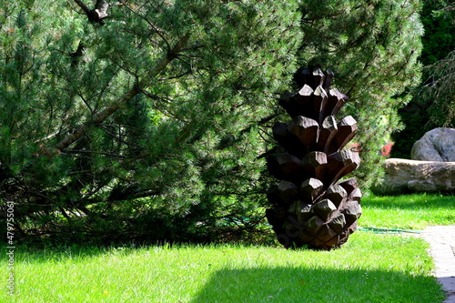 A close up on a massive figurine located in the middle of a public park next to some shrubs that resembles a big yellow nut or acron with a brown cap seen on a sunny summer day on a Polish countryside photo