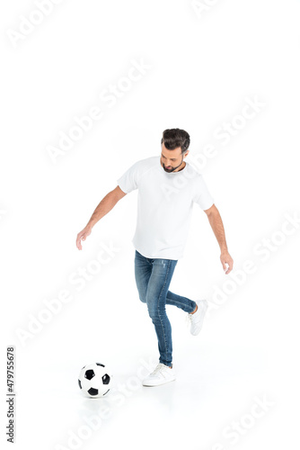 full length view of man in t-shirt and jeans playing football isolated on white.
