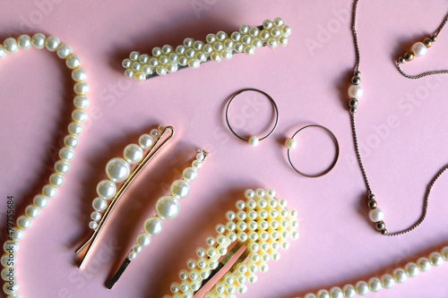 Various pearl jewelry and hair accessories on pink background. Flat lay.