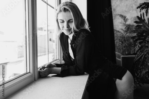 Portrait of a black and white young, pretty European girl emotional in a men's shirt in the bedroom near a large window, smiles, straightens hair. Morning sun, selective focus 