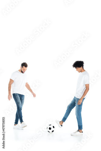 full length view of interracial friends in jeans playing football on white background with copy space.