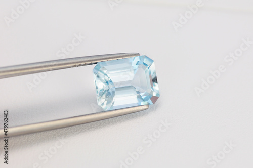 Light blue aquamarine gemstone in tweezer. Octagon shaped, emerald cut, transparent, with small inclusions, unheated, mined in Brazil semiprecious stone setting for jewelry making. White background.