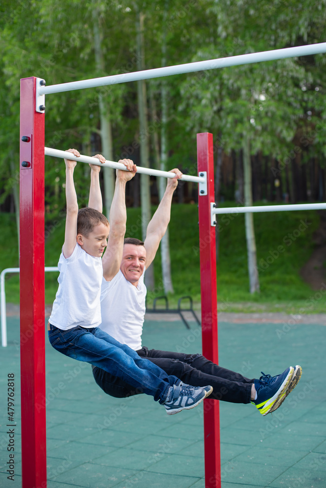 Caucasian man trains a boy on the horizontal bar on the playground. Dad and son go in for outdoor sports. Caucasian man trains a boy on the horizontal bar on the playground. Dad and son go in for outdoor sports.