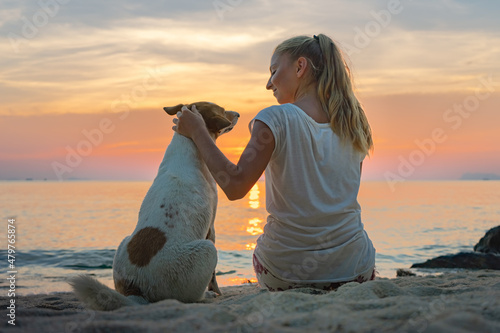 Young woman with dog sitting together on the beach and enjoying the sunset