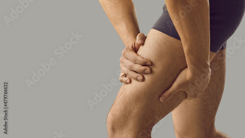 Man feeling pain or having thigh cramp. Sportsman who's suffering from hamstring muscles pain after running, jogging or gym fitness training standing on grey copy space background and touching his leg photo