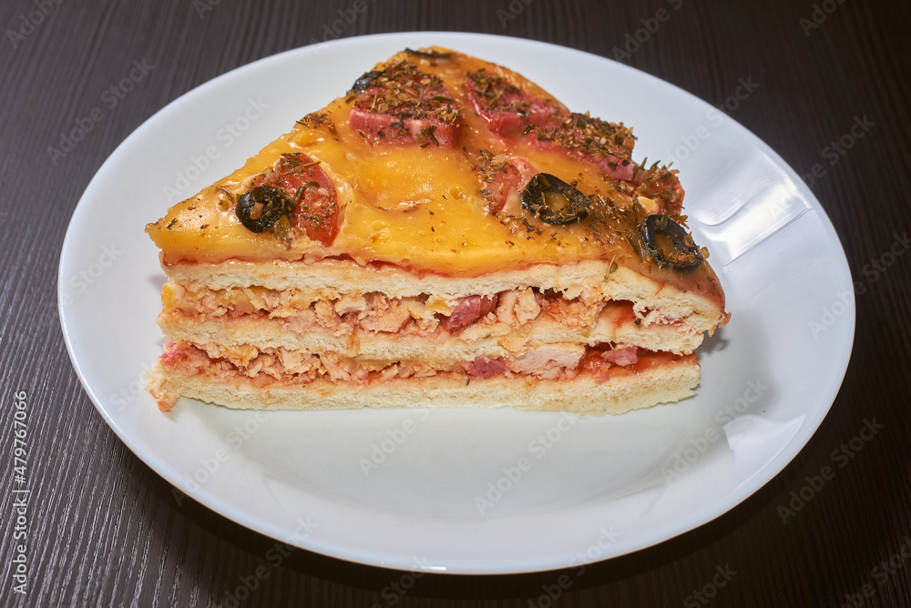 A piece of the three-layer homemade pizza with cheese, sausages, ham and olives. Close-up, selective focus. A piece of the three-layer homemade pizza with cheese, sausages, ham and olives. Close-up, selective focus.