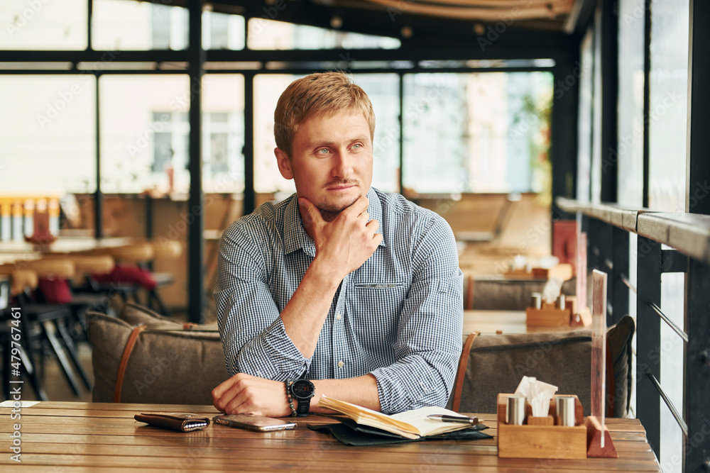 Portrait of adult man that is sitting indoors by the table in the cafe Portrait of adult man that is sitting indoors by the table in the cafe