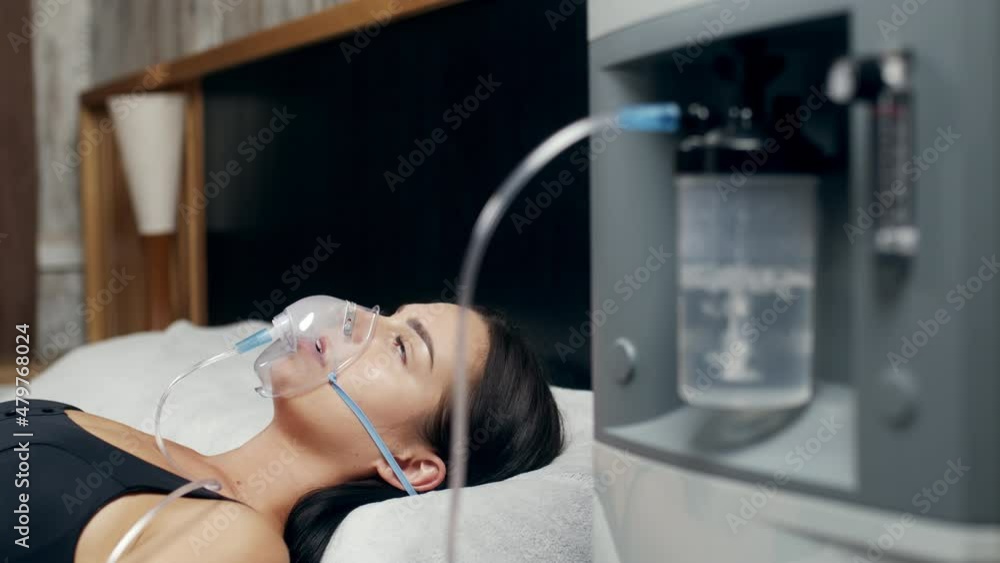 A cinematic close-up of a young woman wearing an oxygen mask being treated for covid-19. Health care, life, home treatment, quarantine concept
