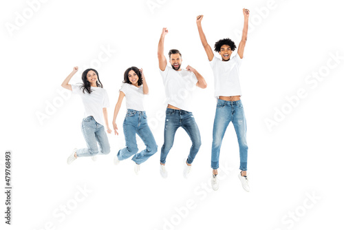 full length view of excited multicultural friends in jeans showing win gesture while levitating isolated on white.