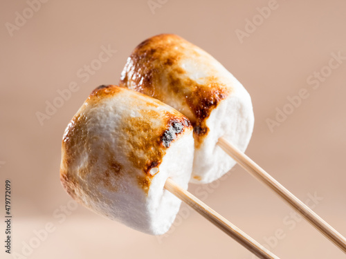 Two sweet marshmallows with baked crust on a brown background.