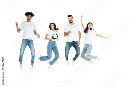 full length view of multiethnic friends with headphones and mobile phones levitating isolated on white.