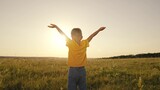 little child with hands raised up at sunset, boy believes in religion in the rays sunlight in the sky, happy family, kid son looks into the distance dawn, boy's summer sunny day, adventure travel fun