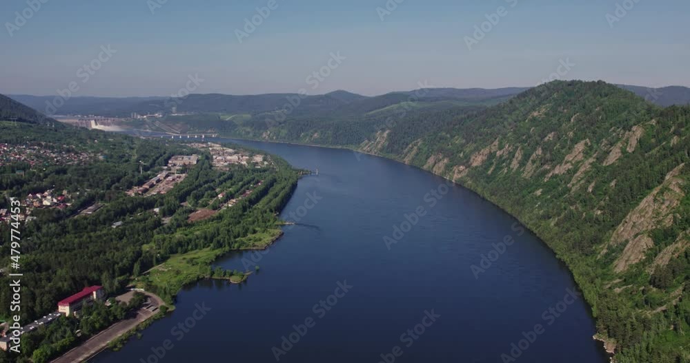 Flying on the drone is a hydroelectric power station on a wide river, lots of green trees and a city Flying on the drone is a hydroelectric power station on a wide river, lots of green trees and a city