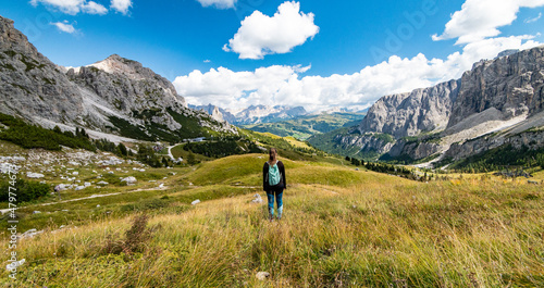Aerial view of female trekker looking at Gardena Pass, Sass da Ciampac, Tor Bornech and Sass dla Luesa, Trentino Alto Adige, Italy. Alpine meadows and Passo Gardena.
