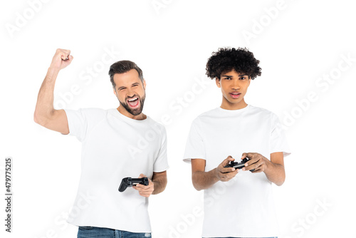 KYIV, UKRAINE - DECEMBER 5, 2021: excited man showing win gesture while gaming with upset african american friend isolated on white.