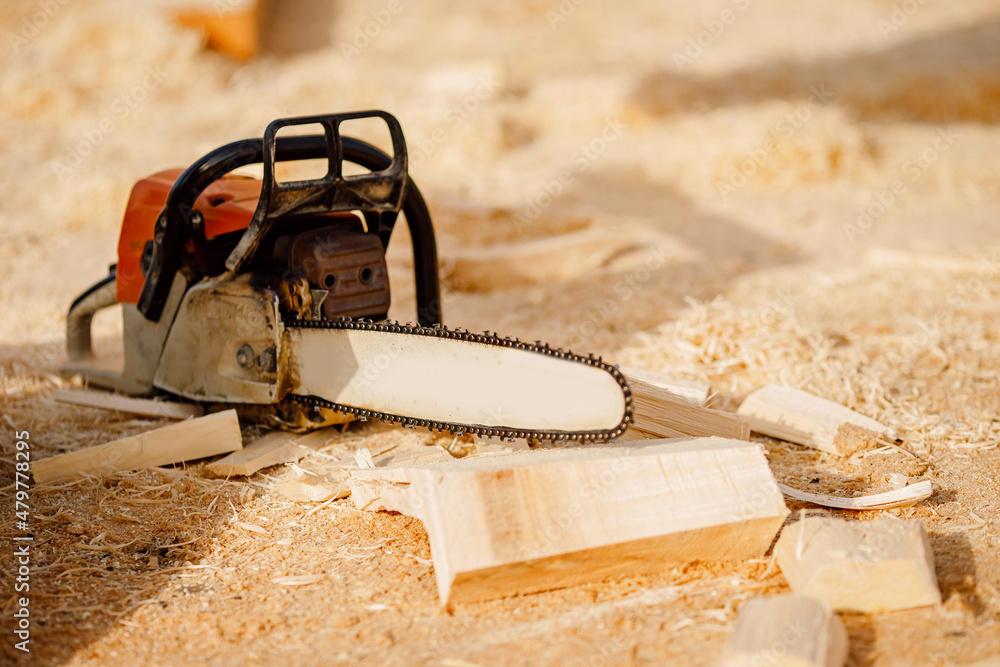 Chainsaw at construction site of wooden houses made of logs lies on background of sawdust
