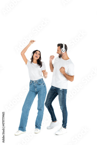 full length view of excited couple in headphones and jeans dancing on white.