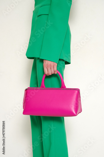 Girl in green suit with pink leather handbag in her hand. Green pants and blazer with fashionable accessory. Vertical photo with white background.