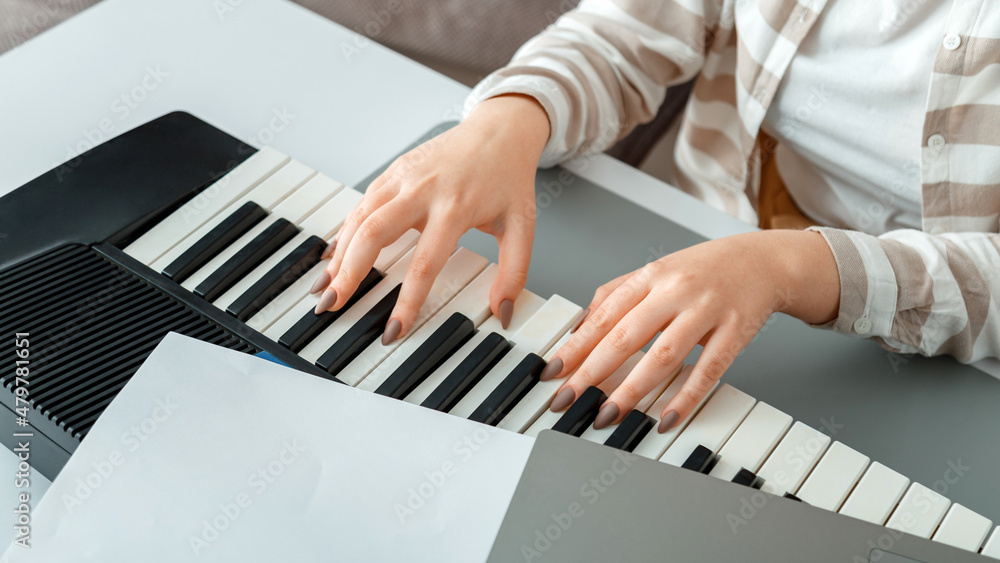 Fototapeta premium Woman playing piano record music on synthesizer using notes and laptop. Female hands musician pianist improves skills playing piano. Online Music education hobby vocals singing. Long web banner.