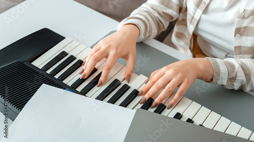 Woman playing piano record music on synthesizer using notes and laptop. Female hands musician pianist improves skills playing piano. Online Music education hobby vocals singing. Long web banner.
