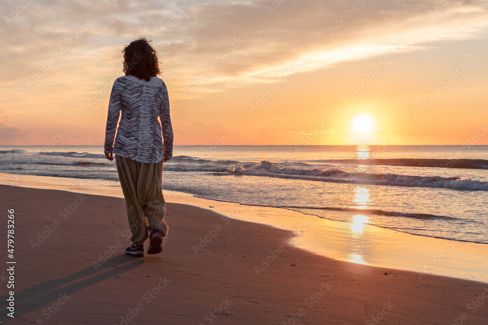 Woman walking when the sun rises on the beach of Serrallo-Delta del Ebro