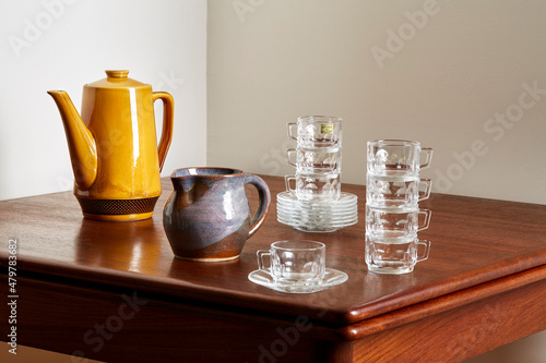 Vintage tableware, handmade ceramic pitcher, amber glazed teapot, and clear glass teacup set. 
