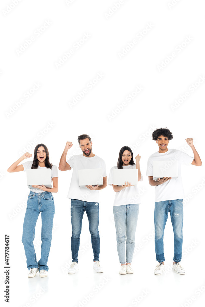 full length view of happy multiethnic friends with laptops showing triumph gesture on white. full length view of happy multiethnic friends with laptops showing triumph gesture on white.