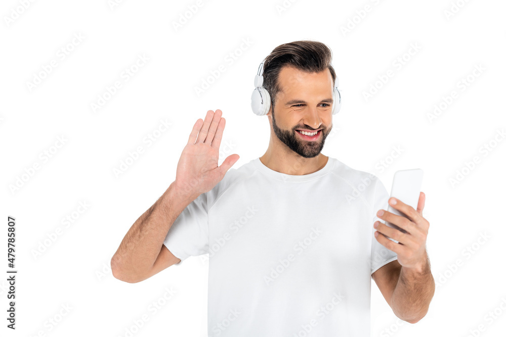 joyful man in headphones waving hand during video call on smartphone isolated on white. joyful man in headphones waving hand during video call on smartphone isolated on white.
