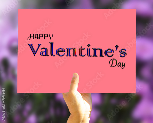 Photos Women's hand holding a postcard of Happy Valentine's Day on blur flower garden b