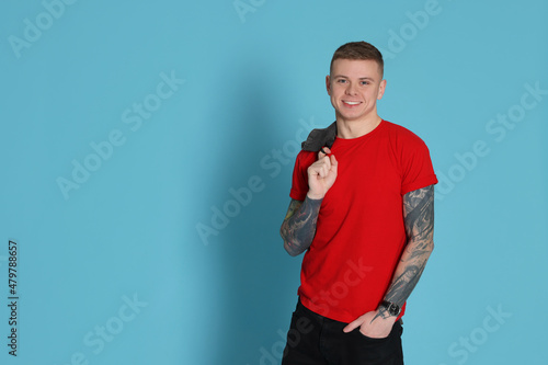 Smiling young man with tattoos on light blue background. Space for text