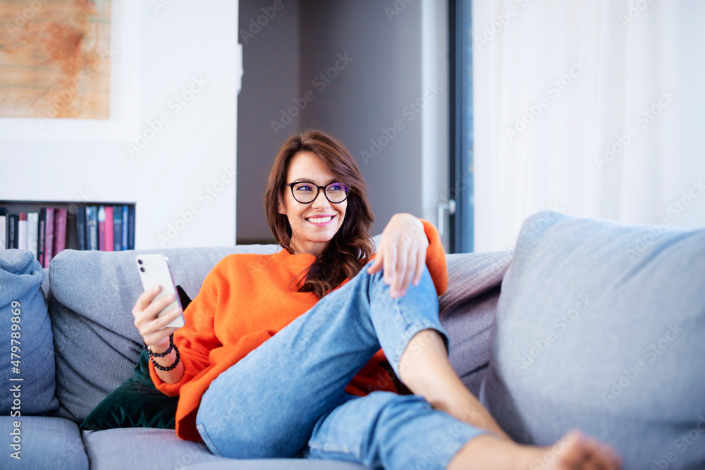 Beautiful woman using smartphone while relaxing on the sofa at home Beautiful woman using smartphone while relaxing on the sofa at home
