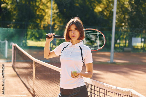 Standing with racket in hand. Female tennis player is on the court at daytime