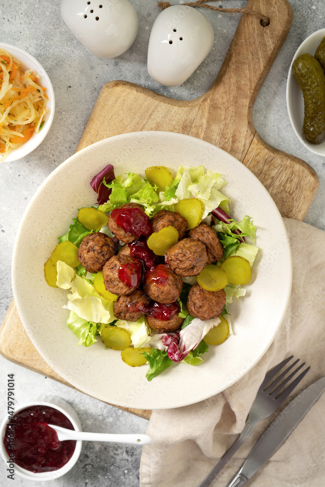 Swedish meatballs with salad, pickled cucumber and lingonberry jam in a bowl. A traditional Scandinavian dish in a ceramic plate on a light gray culinary background. Top view