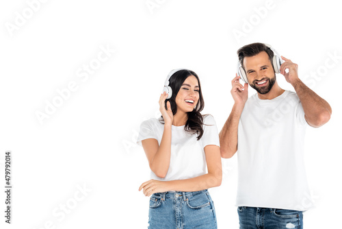 happy man looking at camera while listening music in headphones with cheerful woman isolated on white.