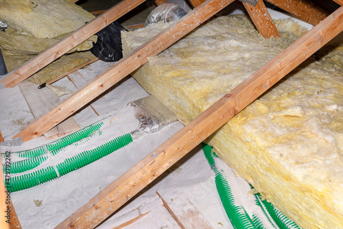 Expanded perlite and mineral wool insulation laid on pipes in domestic ventilation with heat recovery, green pipes laid on the roof truss.