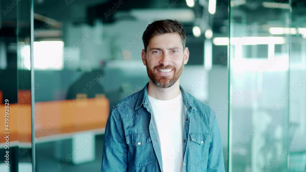 Portrait of a young handsome bearded man. A creative office worker who stands in the modern world and smiles. Happy male employee, architect or designer in casual. at work looking at camera smiling Portrait of a young handsome bearded man. A creative office worker who stands in the modern world and smiles. Happy male employee, architect or designer in casual. at work looking at camera smiling