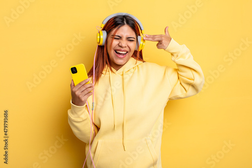 hispanic woman looking unhappy and stressed, suicide gesture making gun sign. headphones and smartphone concept photo