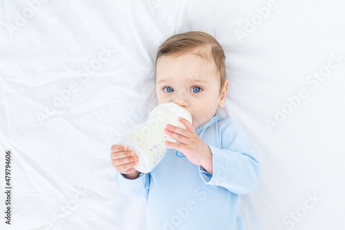 baby boy with a bottle of milk on the bed before going to bed in a blue bodysuit, baby food concept