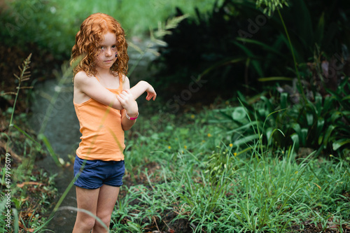 Young redhead girl standing in bushland holding her arm photo