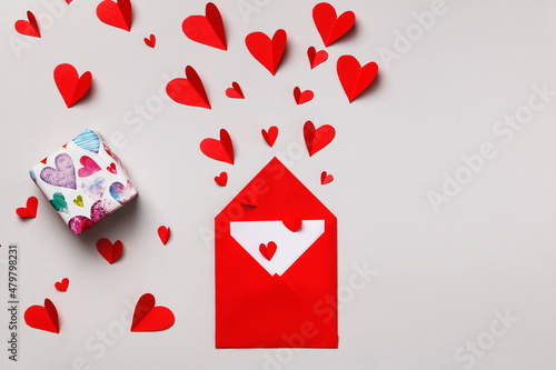 Love letter for Valentine's Day. Red paper envelope with a note inside, a box with a gift and hearts on a gray pastel background.