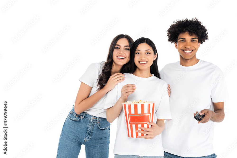smiling african american man clicking tv channels near happy interracial women with bucket of popcorn isolated on white. smiling african american man clicking tv channels near happy interracial women with bucket of popcorn isolated on white.