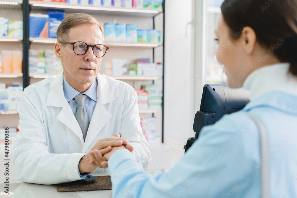 Mature male pharmacist doctor supporting, sympathizing female customer client buyer, listening attentively to her medical complaints in drugstore
